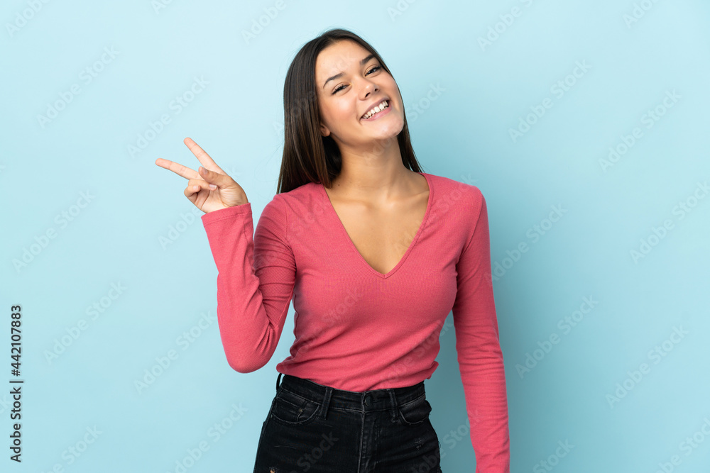 Teenager girl isolated on blue background smiling and showing victory sign Teenager girl isolated on blue background smiling and showing victory sign