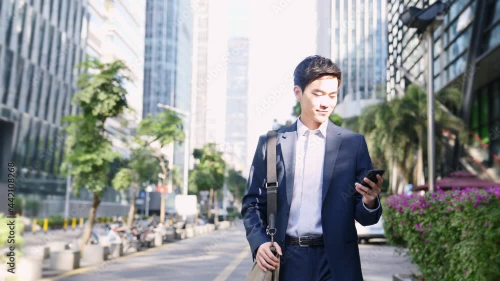 young asian business man commuter looking at cellphone while walking on street in downtown financial district of modern city young asian business man commuter looking at cellphone while walking on street in downtown financial district of modern city