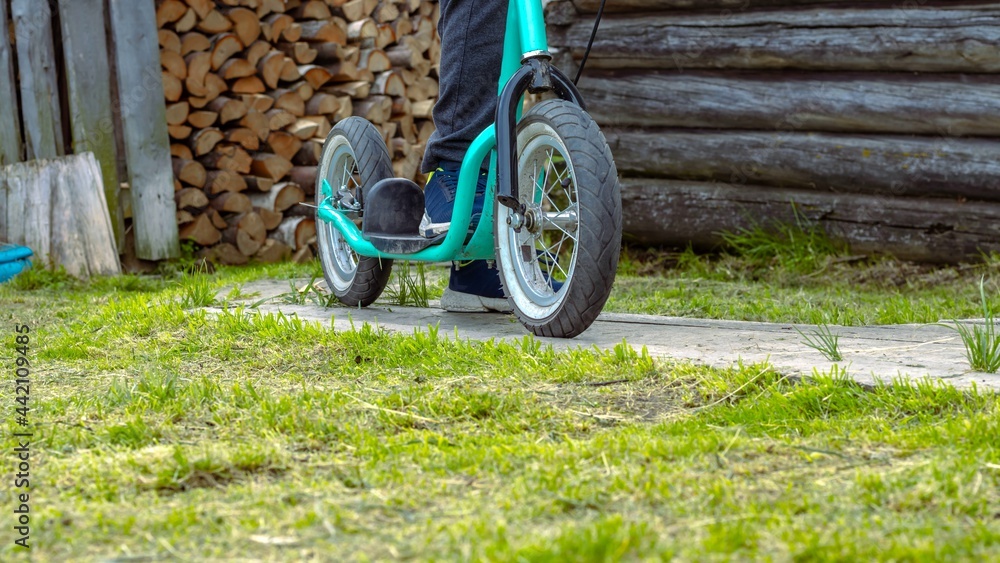 Child's feet on a scooter with large wheels on the background of a village house. Active lifestyle