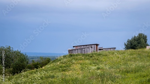 Old wooden buildings on a green hill against the background of a gray cloudy sky. Country life