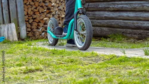 Child's feet on a scooter with large wheels on the background of a village house. Active lifestyle