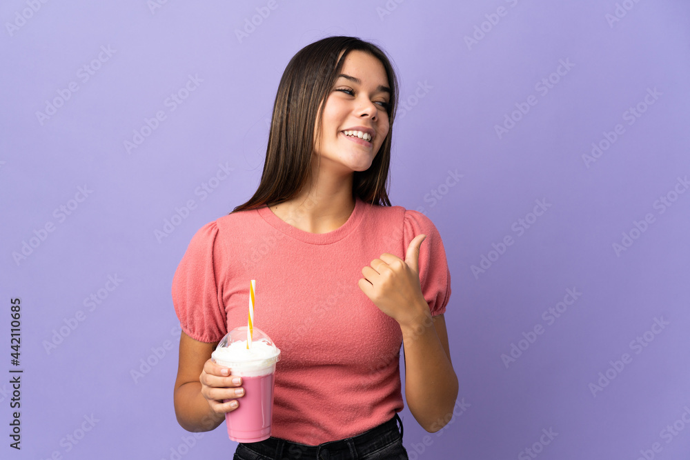 Teenager girl holding a strawberry milkshake pointing to the side to present a product Teenager girl holding a strawberry milkshake pointing to the side to present a product