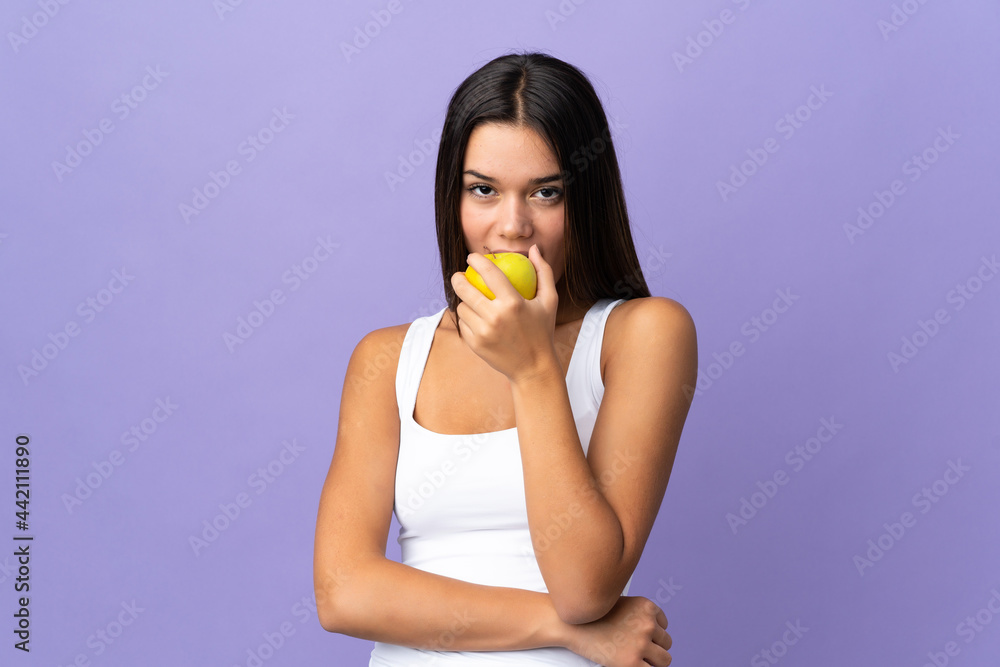 Teenager girl isolated on purple background eating an apple Teenager girl isolated on purple background eating an apple