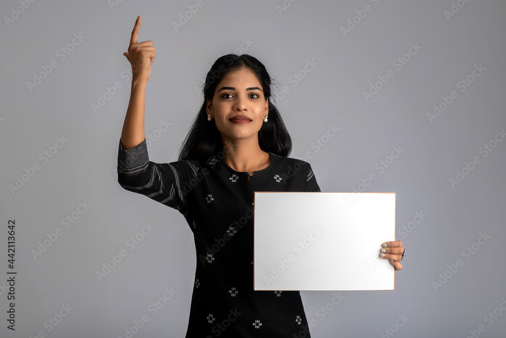 A young woman or businesswoman holding a signboard in her hands on a gray background. A young woman or businesswoman holding a signboard in her hands on a gray background.