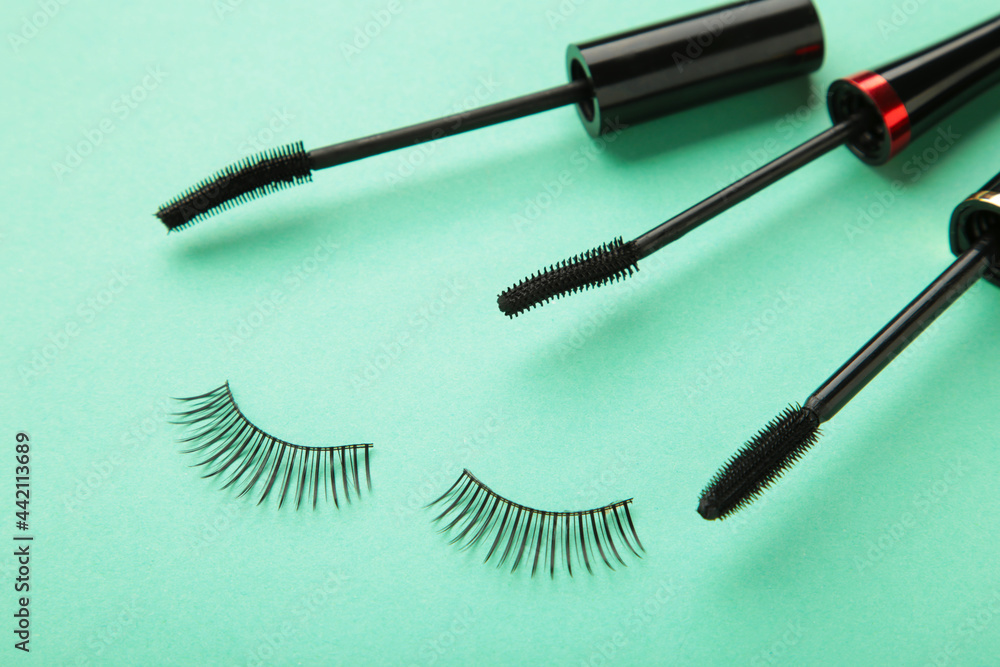 Close up of black eyeliners and mascara brush on mint background