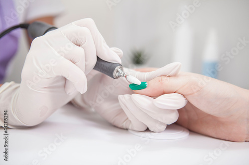 Close up of manicurist removing nail gel with nail file drill