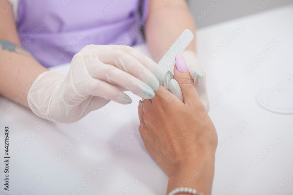 Cropped shot of manicurist filing thumb fingernail of female client Cropped shot of manicurist filing thumb fingernail of female client