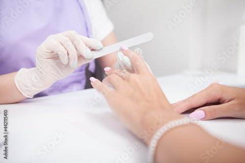 Cropped close up of professional manicurist filing nails of female client