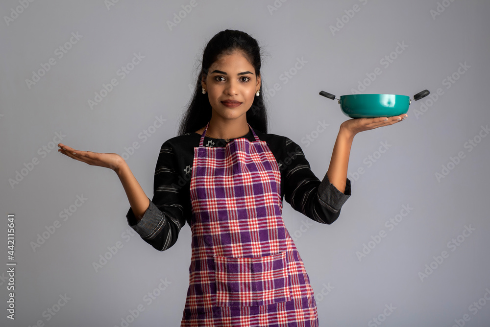 Young girl holding and posing with kitchen utensils pan on a grey background Young girl holding and posing with kitchen utensils pan on a grey background