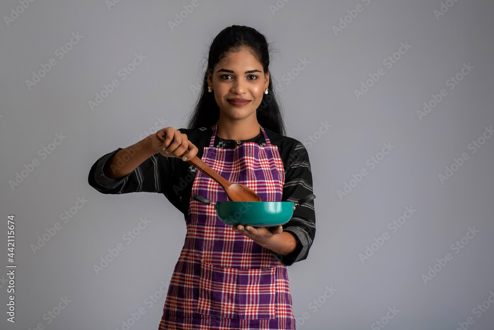 Young girl holding and posing with kitchen utensils spatula and pan on a grey background Young girl holding and posing with kitchen utensils spatula and pan on a grey background