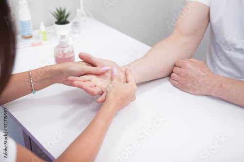 Cropped shot of manicurist massaging hands of male client with hand cream