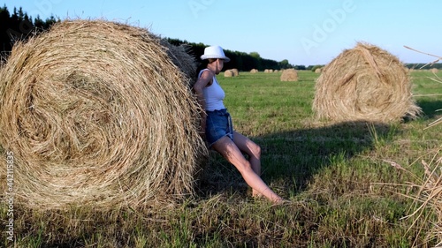 beautiful young girl in a hat pushes a haystack. Rural area. Feminist strong woman concept