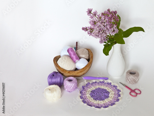 Spring still life with needlework and crochet. Hand crochet accessories and beautiful hand knitted round lace doily. A sprig of blooming lilacs in a vase on a white background. Empty space for text
