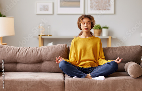 Young mixed race woman meditating with closed eyes  in living room at home photo