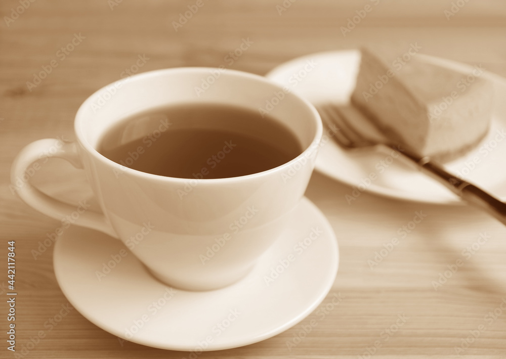 Sepia Image of a Cup of Hot Tea with Blurry Baked Cheesecake in Background Sepia Image of a Cup of Hot Tea with Blurry Baked Cheesecake in Background