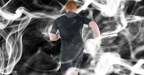 Composition of male rugby player holding rugby ball on black background