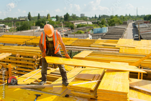 A worker in a safety helmet assembles a formwork from wooden panels photo