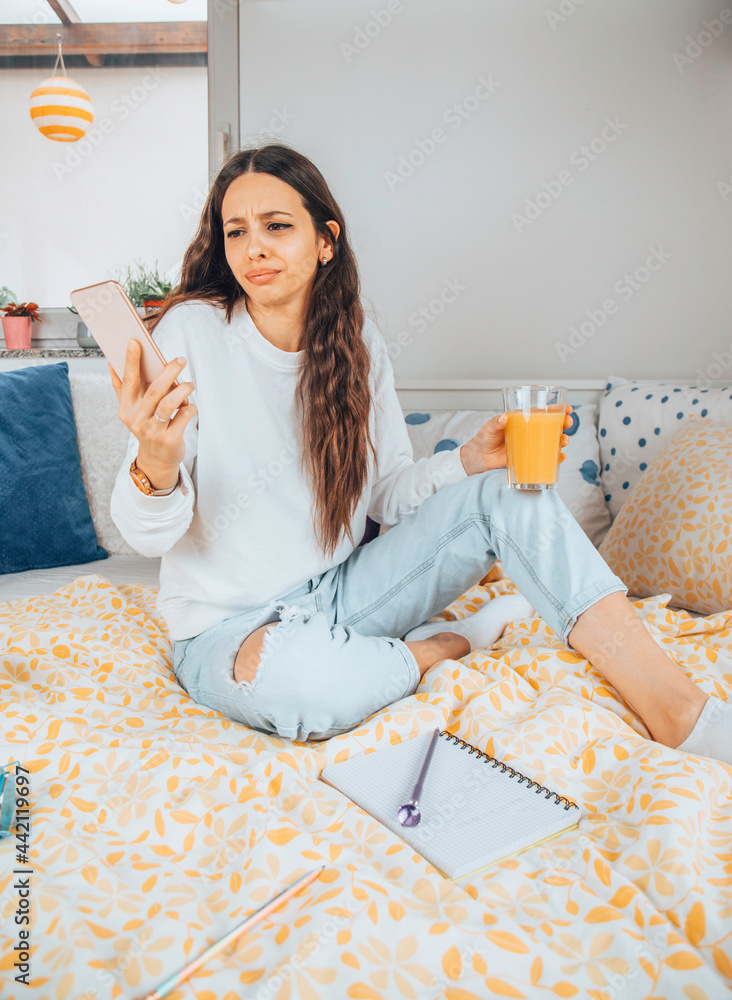Angry woman talking on a cellphone while drinking juice in her bed. Angry woman talking on a cellphone while drinking juice in her bed.