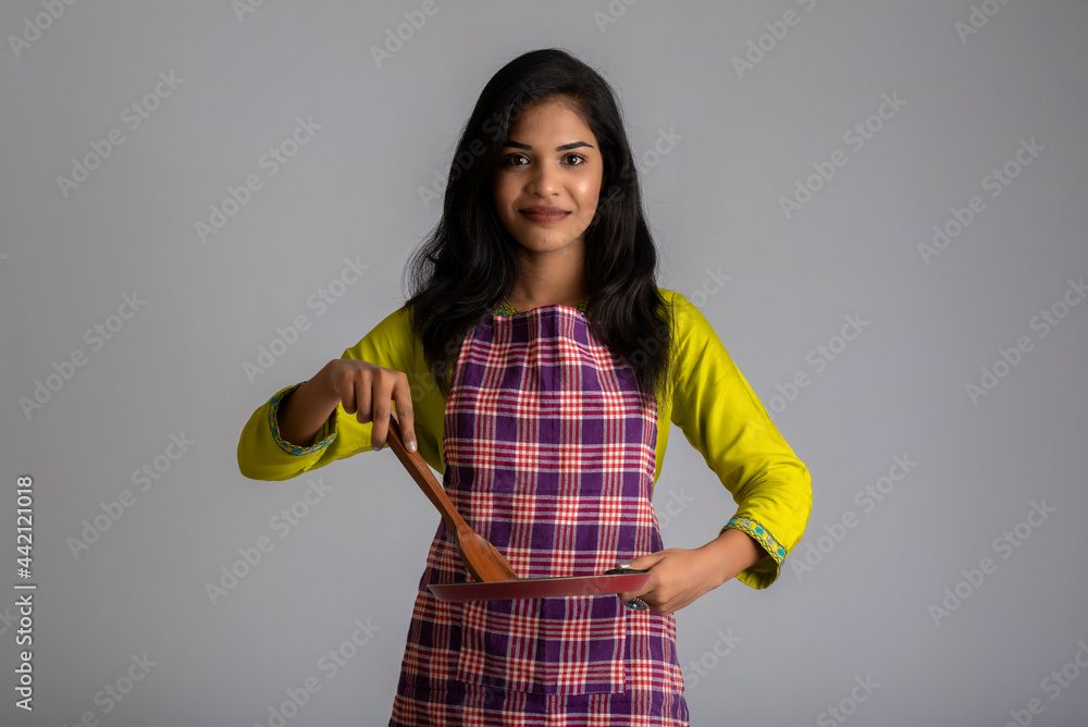 Young girl holding kitchen utensils spatula and pan on a grey background Young girl holding kitchen utensils spatula and pan on a grey background