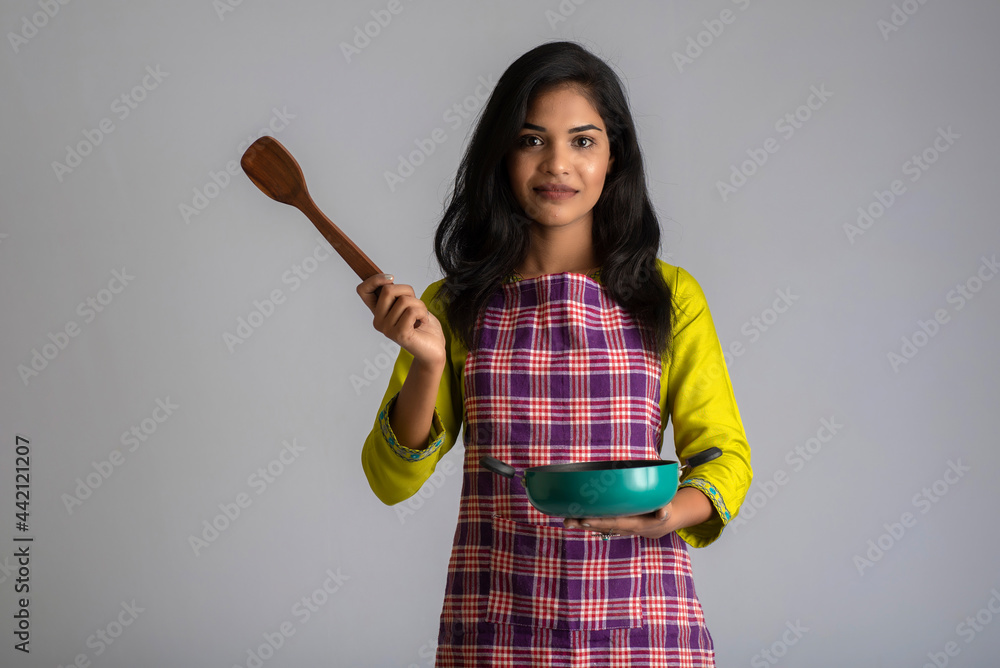 Young girl holding and posing with kitchen utensils on a grey background Young girl holding and posing with kitchen utensils on a grey background