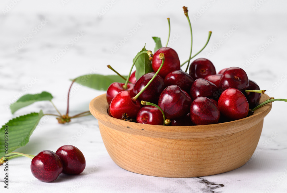 ripe red cherries in a brown wooden plate on a white table ripe red cherries in a brown wooden plate on a white table
