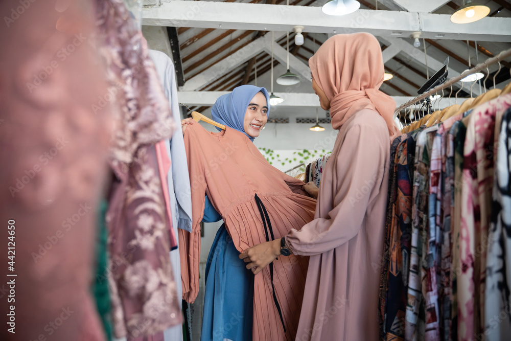 asian veiled waitresses while serving female shoppers choosing clothes on hangers in boutique shops