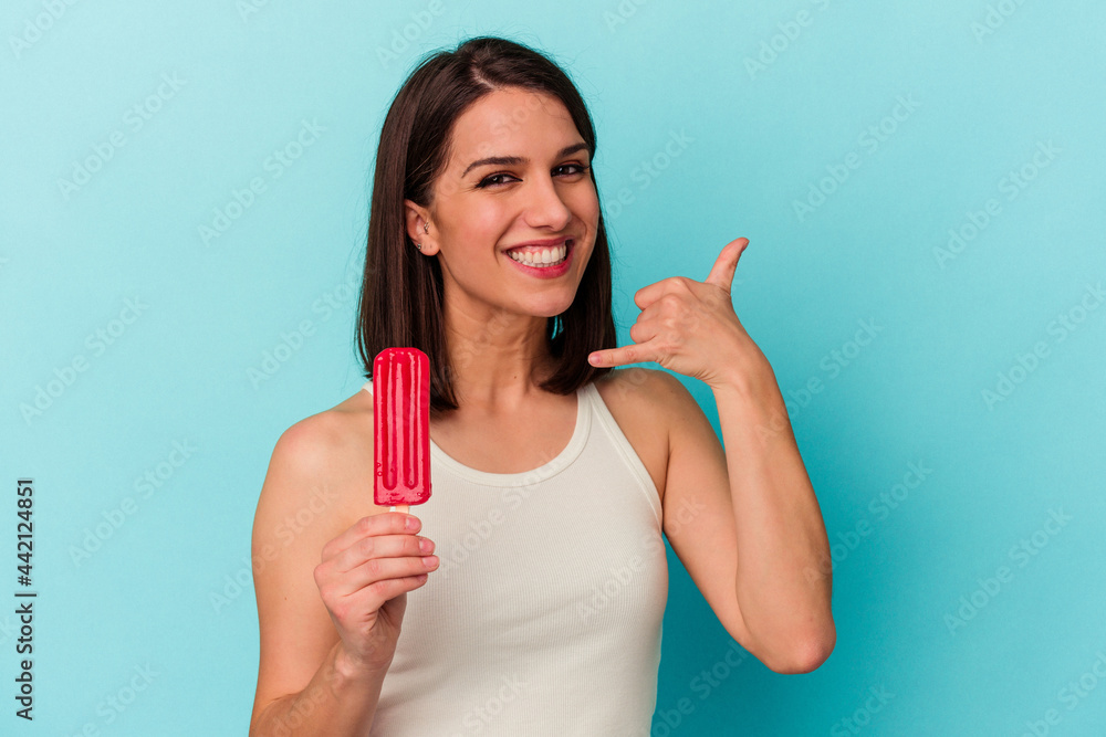 Young caucasian woman holding an ice cream isolated on blue background showing a mobile phone call gesture with fingers. Young caucasian woman holding an ice cream isolated on blue background showing a mobile phone call gesture with fingers.