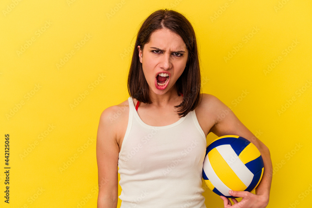 Young caucasian woman playing volleyball isolated on yellow background screaming very angry and aggressive.