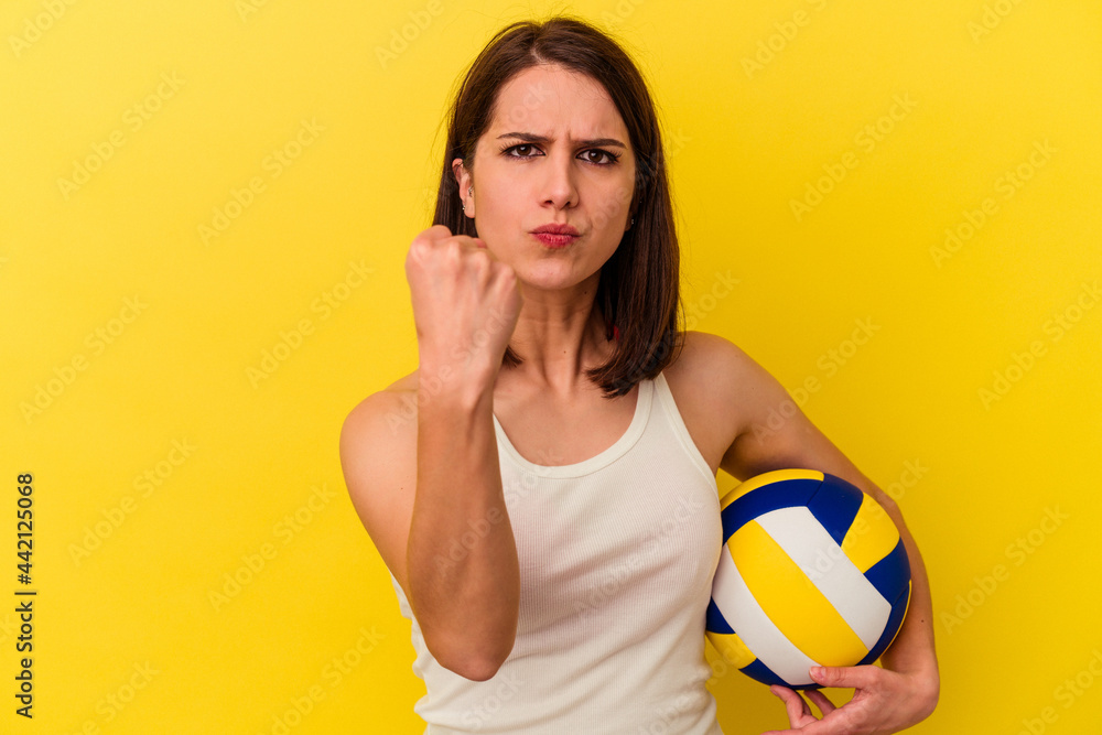 Young caucasian woman playing volleyball isolated on yellow background showing fist to camera, aggressive facial expression.