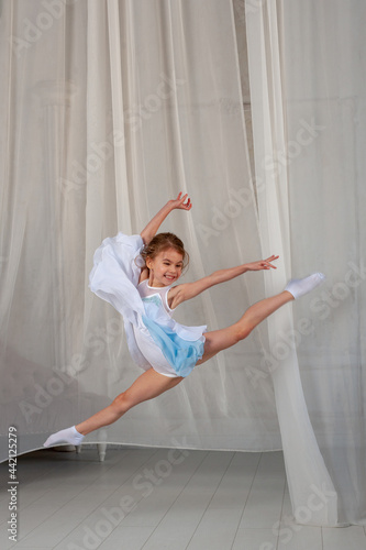 Fototapeta Naklejka Na Ścianę i Meble -  Pretty girl jumping in a dress on the background of a white curtain. children's sports concept.