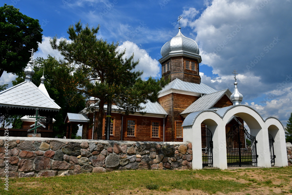 A close up on an old wooden Orthodox church with a beautiful metal dome or tower and surrounded with a tall wall made out of rock or stone and a neat gateway leading to the object seen in Poland