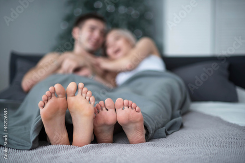 Close-up of male and female legs. The loving couple lies and embraces on the bed under a gray blanket. Light room.