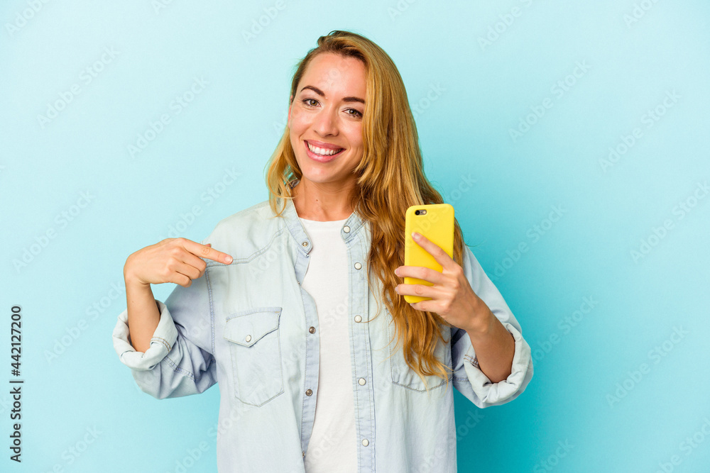 Caucasian woman holding mobile phone isolated on blue background person pointing by hand to a shirt copy space, proud and confident Caucasian woman holding mobile phone isolated on blue background person pointing by hand to a shirt copy space, proud and confident