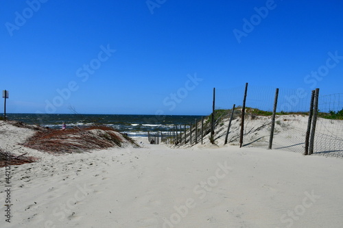 A view of a sandy beach located next to the Baltic Sea with hilltops visible and wooden poles attached to metal fences separating Polish land from the Russian Federation seen on a sunny day 