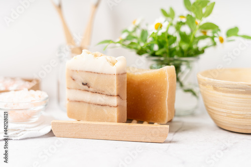 Natural bathroom and home spa tools. Zero waste sustainable lifestyle concept. Natural soap bar in wooden soap dish, cotton pads and swabs, flowers, bamboo toothbrush. White background, copy space