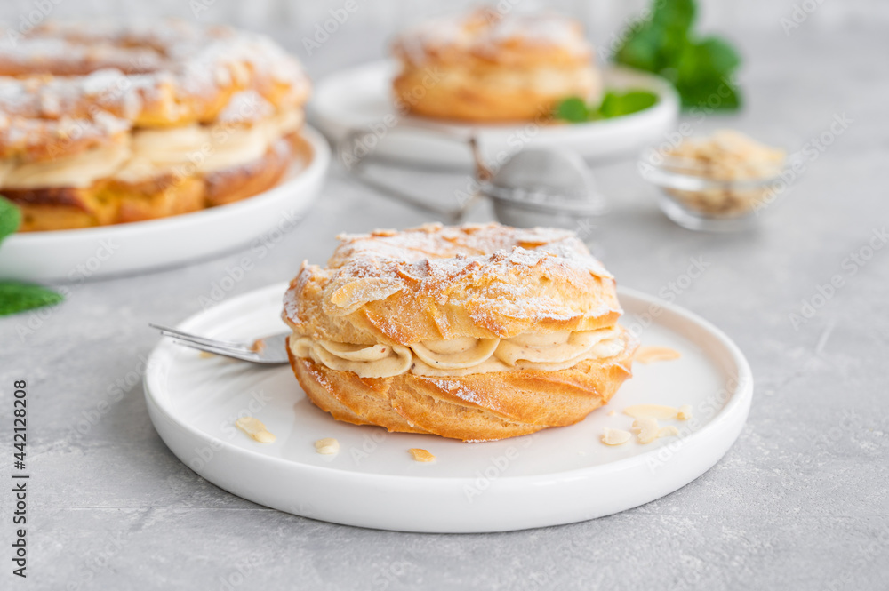 French traditional cake Paris Brest with praline cream, powdered sugar and almond petals on top on a gray concrete background. Copy space.