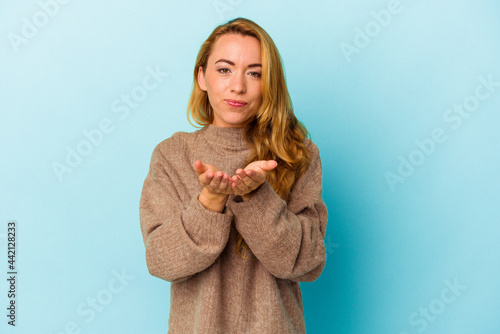 Caucasian woman isolated on blue background holding something with palms, offering to camera.