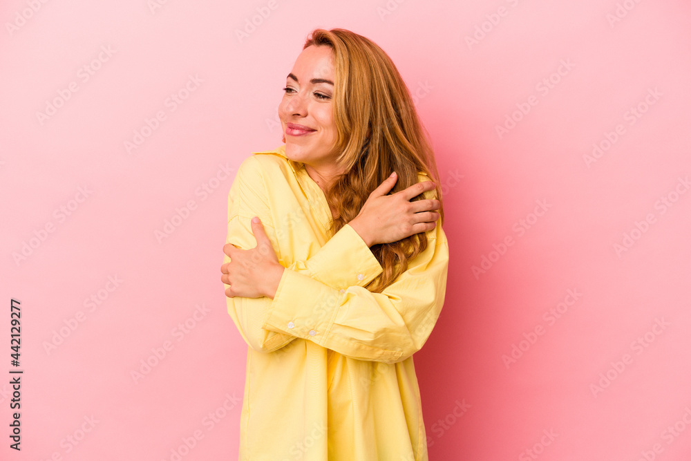 Caucasian blonde woman isolated on pink background hugs, smiling carefree and happy.