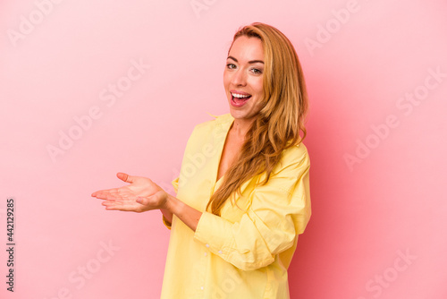 Caucasian blonde woman isolated on pink background holding a copy space on a palm.
