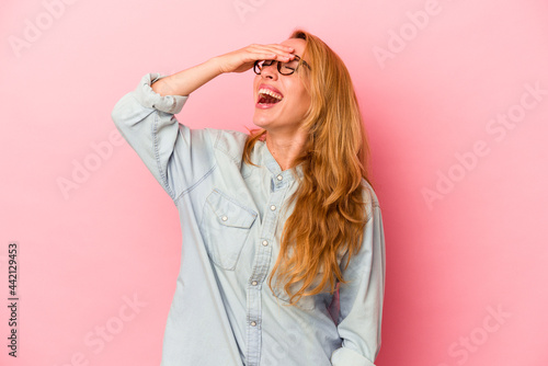 Caucasian blonde woman isolated on pink background laughs joyfully keeping hands on head. Happiness concept.