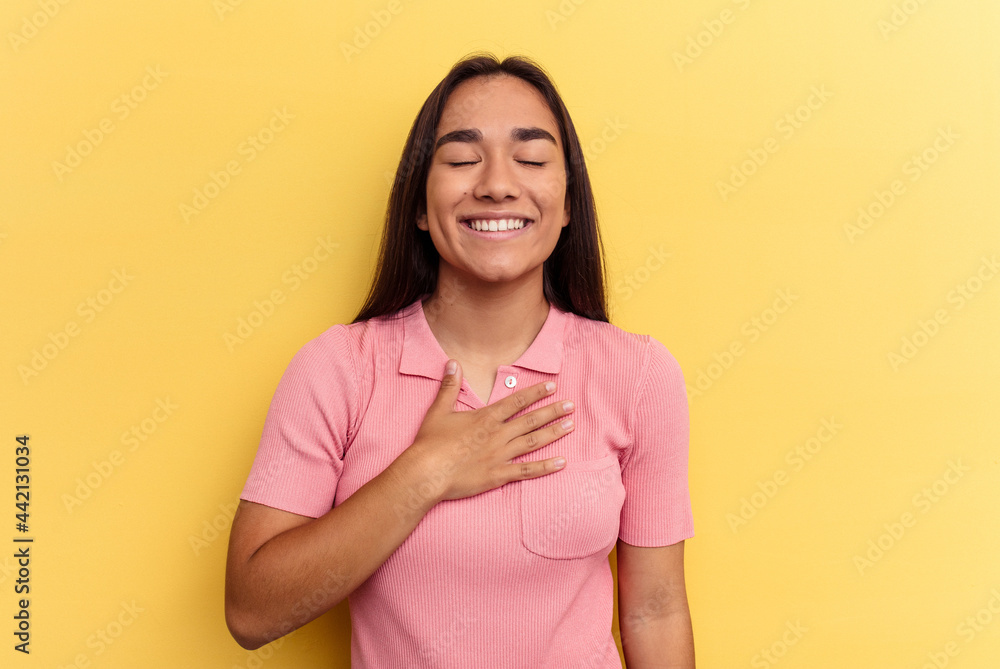 Obraz premium Young mixed race woman isolated on yellow background laughs out loudly keeping hand on chest.