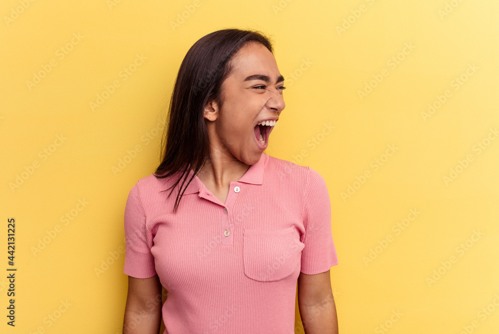 Fototapeta premium Young mixed race woman isolated on yellow background shouting very angry, rage concept, frustrated.