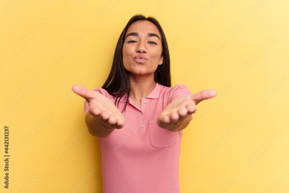 Young mixed race woman isolated on yellow background folding lips and holding palms to send air kiss. Young mixed race woman isolated on yellow background folding lips and holding palms to send air kiss.