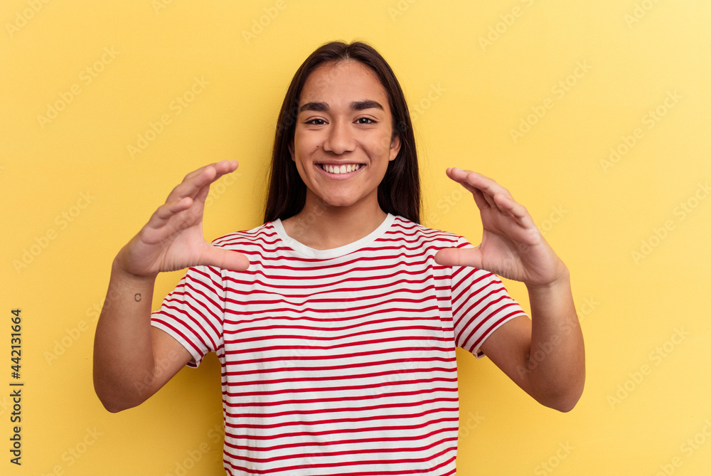 Young mixed race woman isolated on yellow background holding something with palms, offering to camera. Young mixed race woman isolated on yellow background holding something with palms, offering to camera.