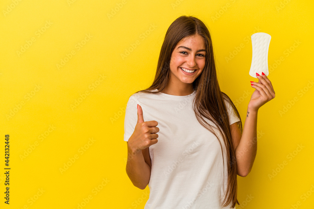 Young caucasian woman holding a compress isolated on yellow background smiling and raising thumb up Young caucasian woman holding a compress isolated on yellow background smiling and raising thumb up