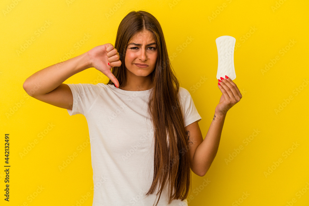 Young caucasian woman holding a compress isolated on yellow background showing a dislike gesture, thumbs down. Disagreement concept. Young caucasian woman holding a compress isolated on yellow background showing a dislike gesture, thumbs down. Disagreement concept.