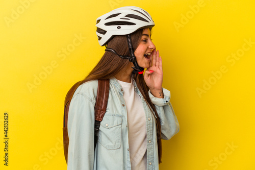 Young student caucasian woman wearing a bike helmet isolated on yellow background shouting and holding palm near opened mouth. © Asier