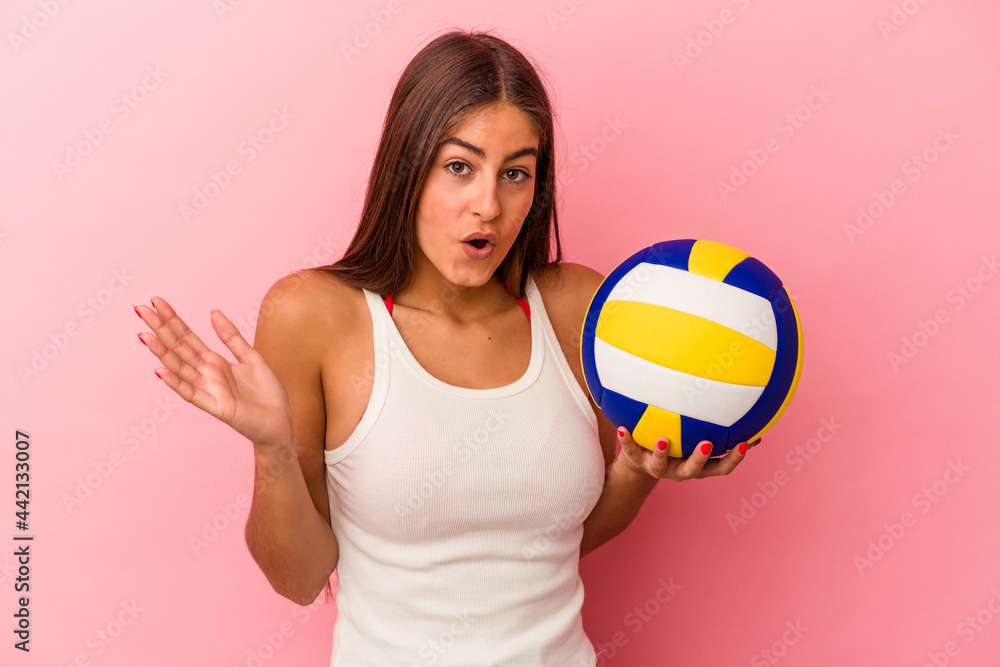Young caucasian woman holding a volleyball ball isolated on pink background surprised and shocked.