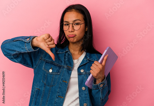 Young venezuelan woman holding a tablet isolated on pink background showing a dislike gesture, thumbs down. Disagreement concept.
