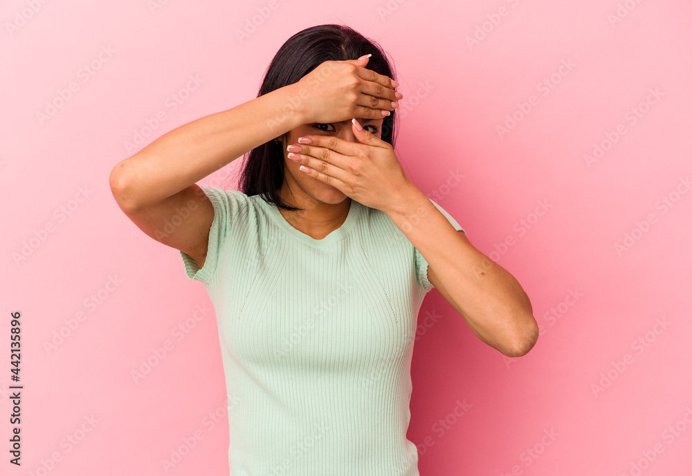 Young Venezuelan woman isolated on pink background blink at the camera through fingers, embarrassed covering face. Young Venezuelan woman isolated on pink background blink at the camera through fingers, embarrassed covering face.